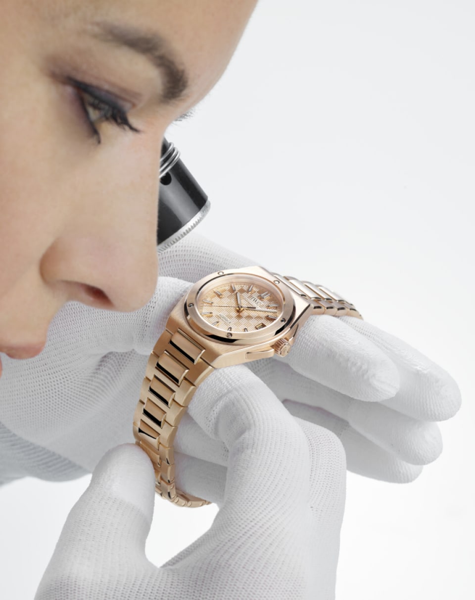 Female watchmaker with loupe and white gloves examining the IW324903 Ingenieur Automatic 35 with gold plated dial, 18 ct 5N gold case and bracelet.