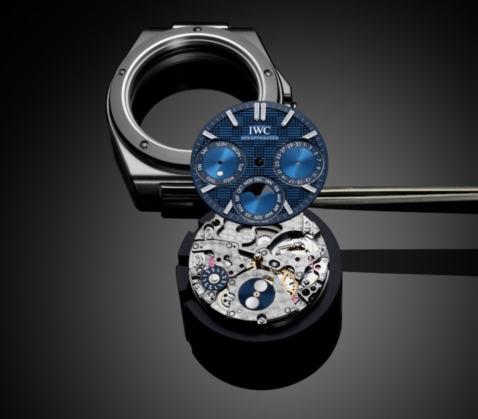 Stainless steel case and blue dial watch parts of IWC Ingenieur Perpetual Calendar 41 with precision tool on black surface.