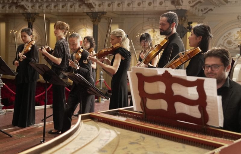 Multiple members of the Amsterdam Baroque Orchestra preparing to perform,Multiple members of the Amsterdam Baroque Orchestra preparing to perform